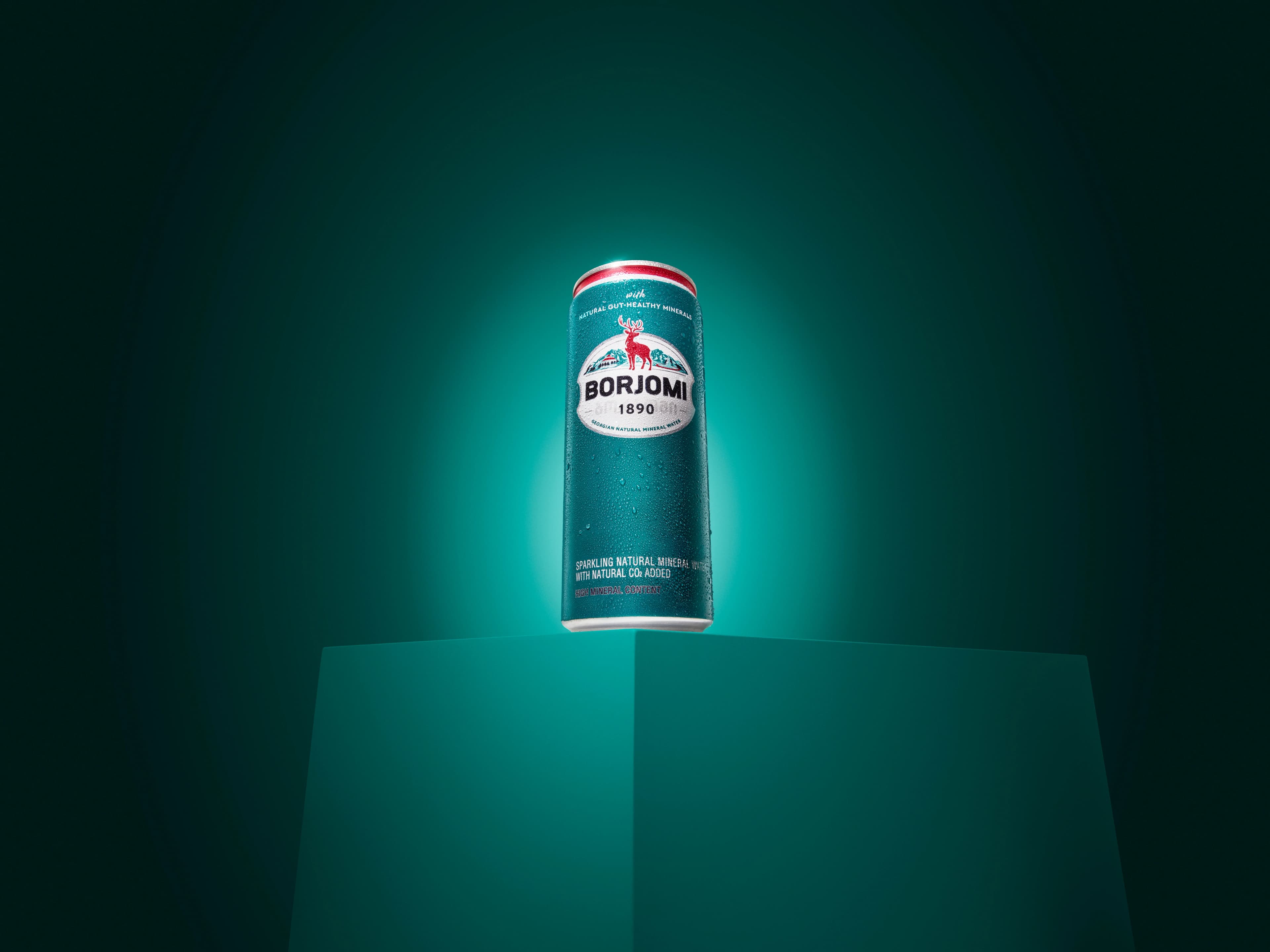 Borjomi glass bottle and can with ice water glasses on a marble table, teal background