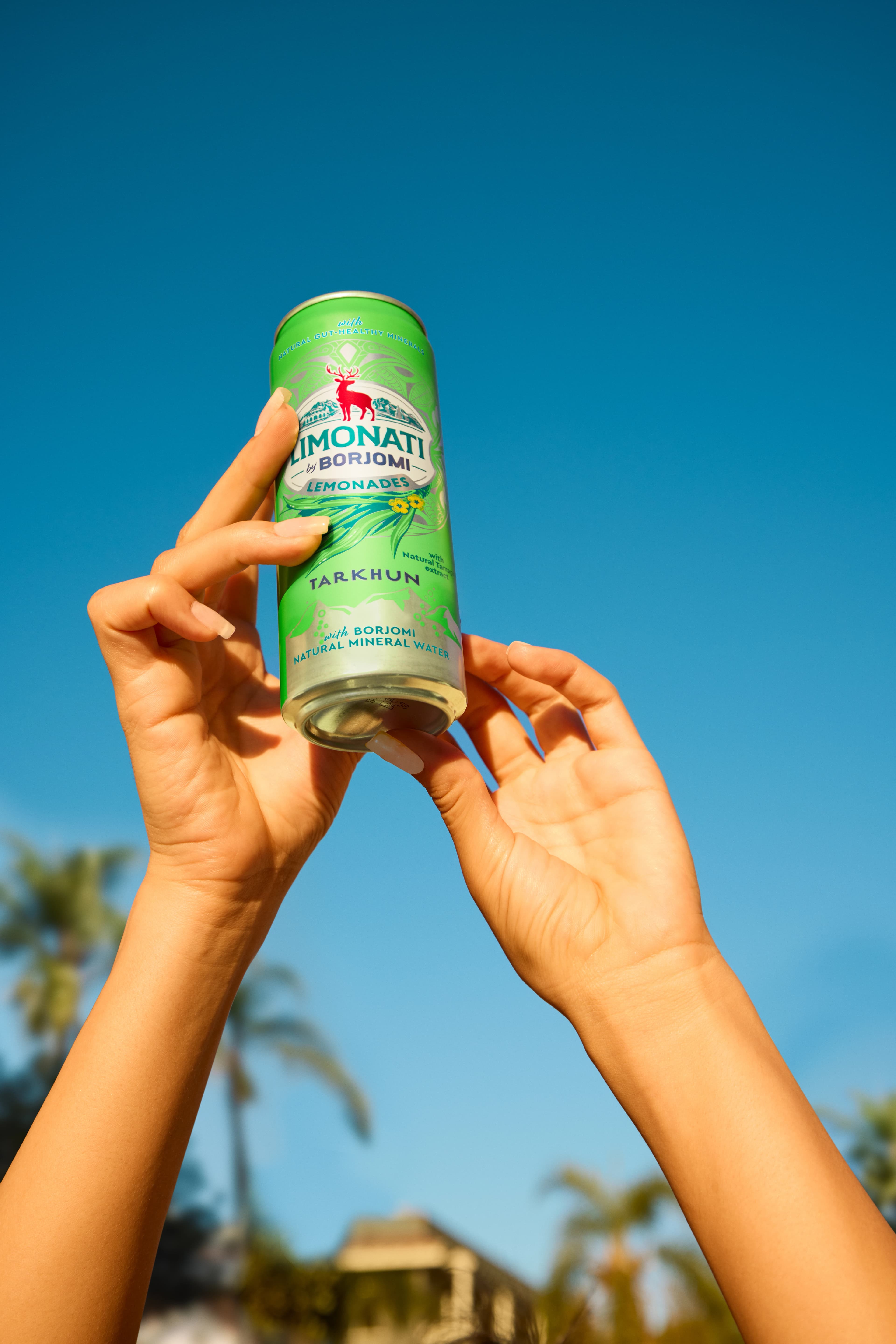 Man holding up a Borjomi can against a clear blue sky