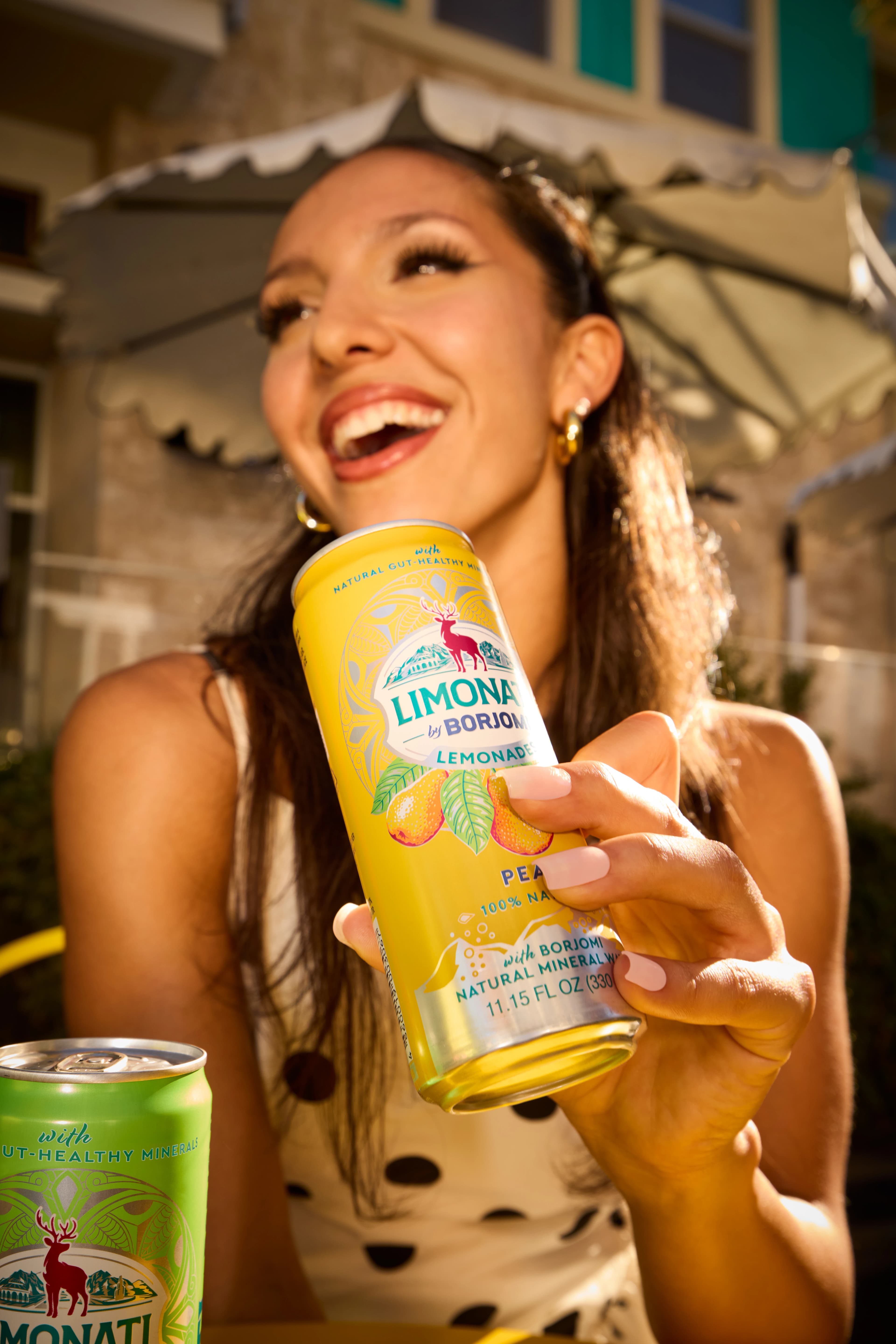 Hands holding a Limonati by Borjomi Adjarian Mandarin can with a squeezed orange above it