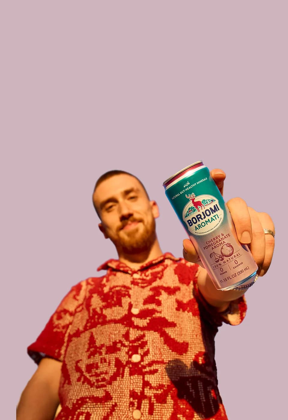 Man holding a Borjomi Aromati cherry pomegranate can on a pink background