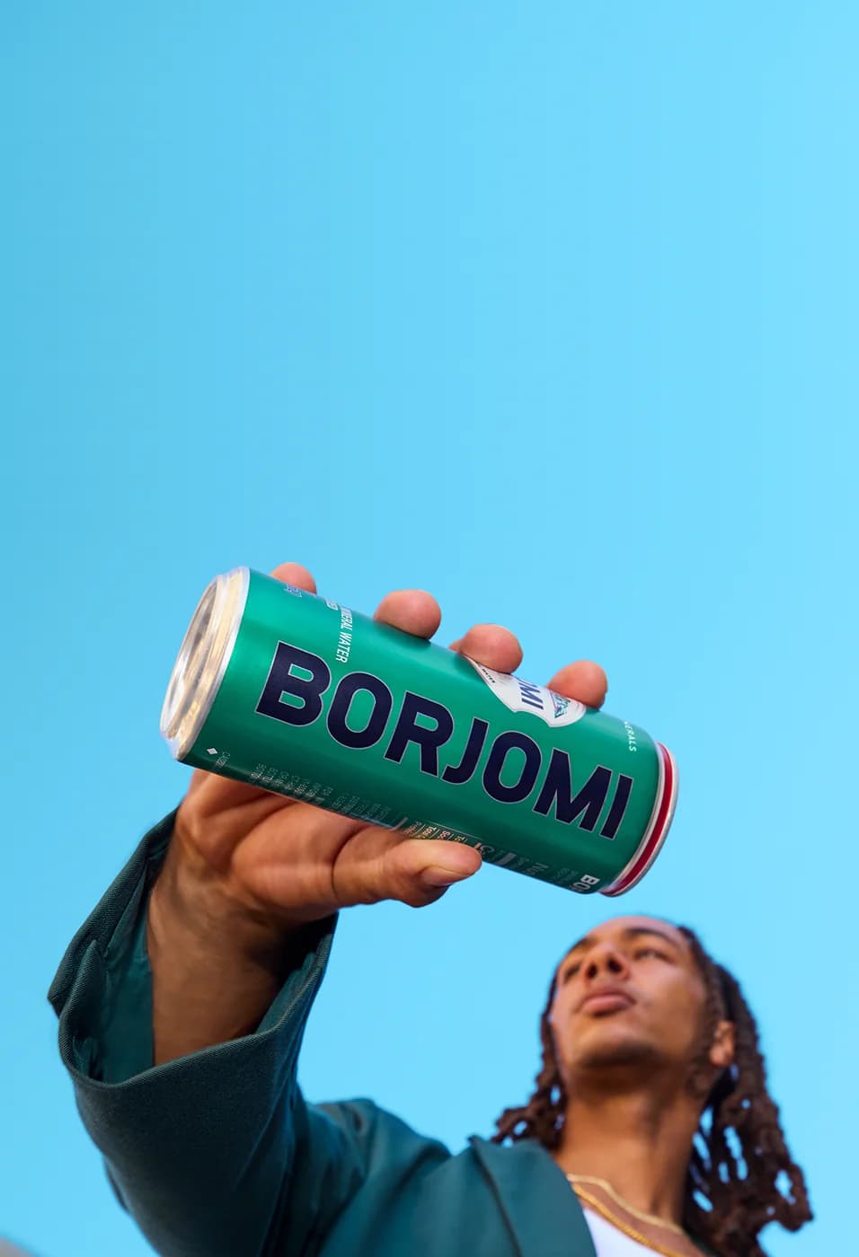 Person holding a Borjomi sparkling water can against a light blue sky