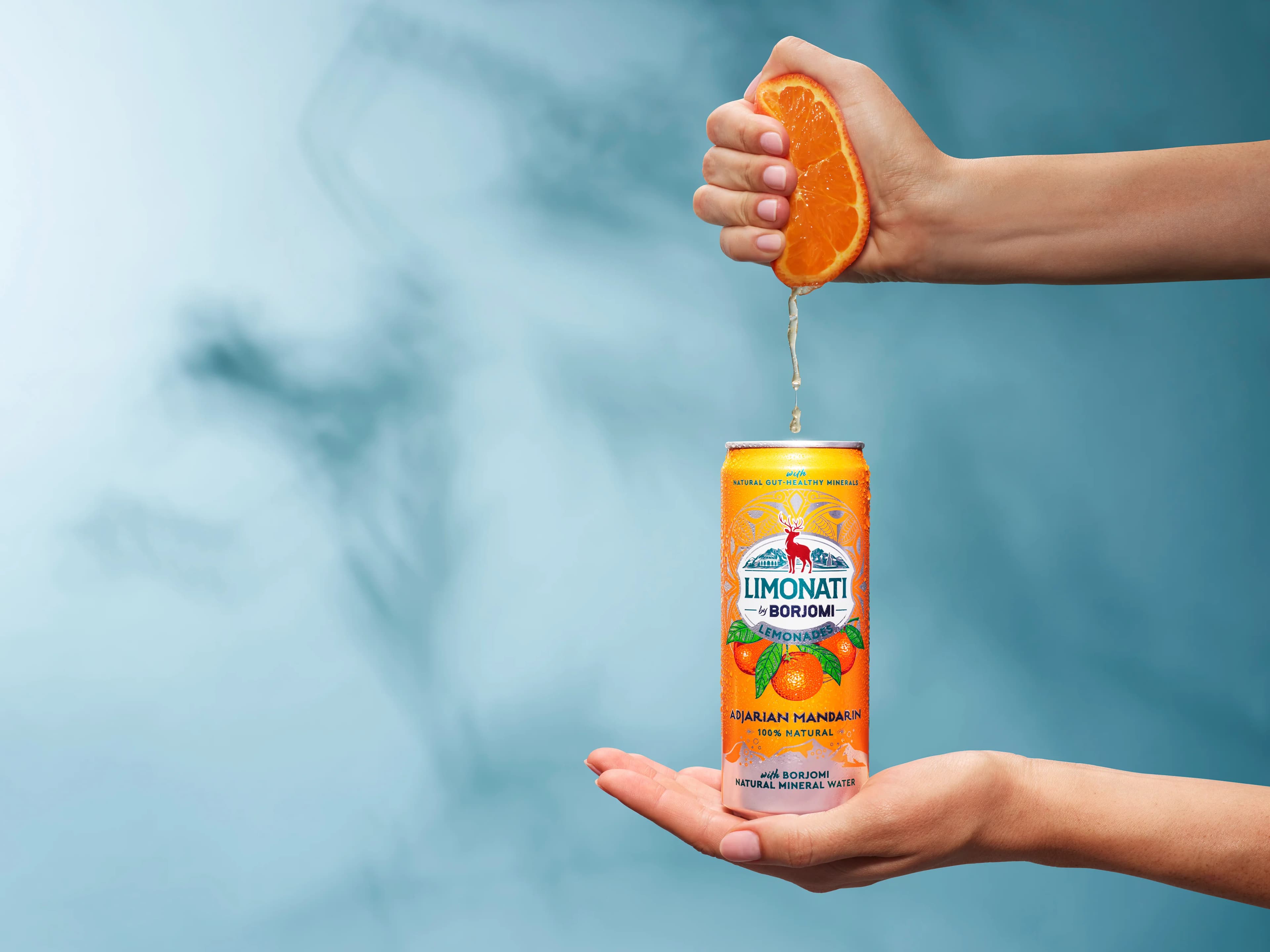 Hands holding a Limonati by Borjomi Adjarian Mandarin can with a squeezed orange above it