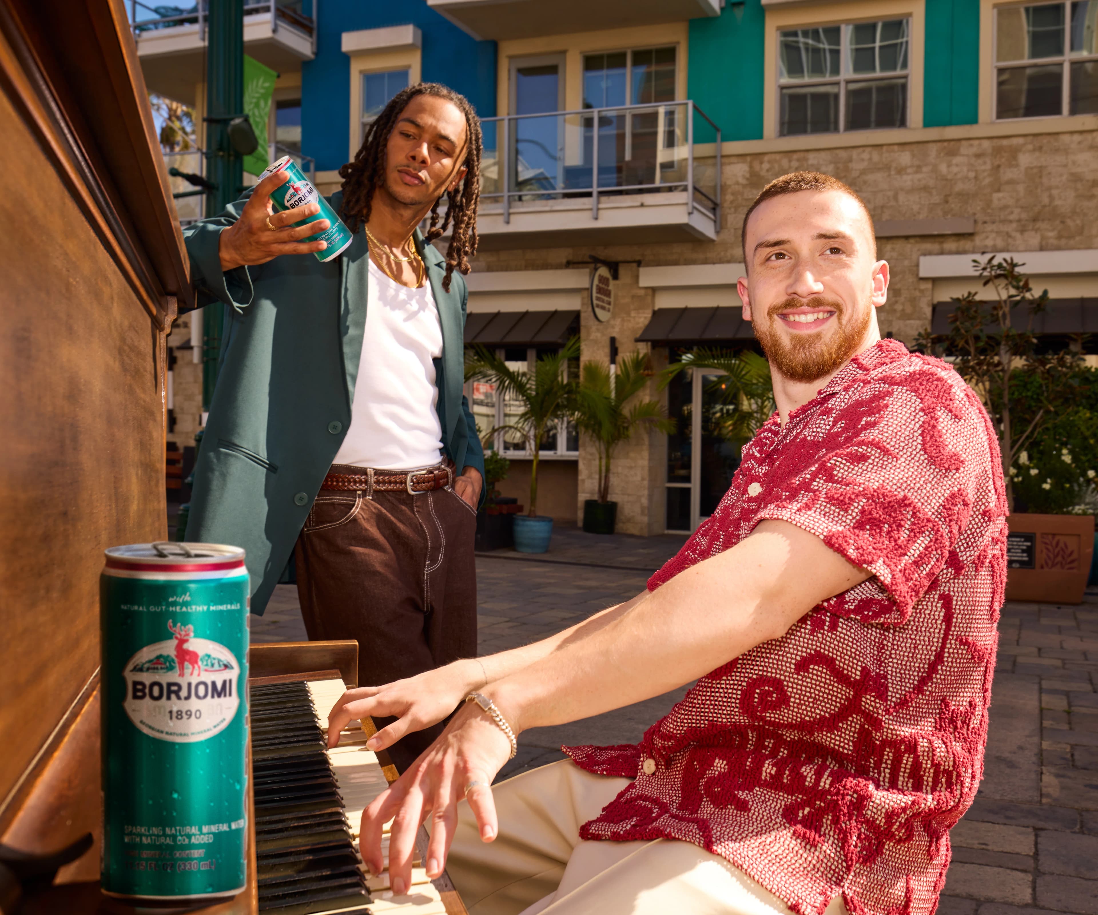 Person in a floral shirt holding a Borjomi can outdoors